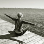 Happiness of freedom, healthy lifestyle, leisure and relax near the water, suburban rest, the woman reaches for the sunlight and breathe freshness of nature, she sits on the pier overlooking the blue water